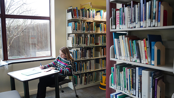 A student sits at a desk and writes on a piece of paper in the Architecture Library
