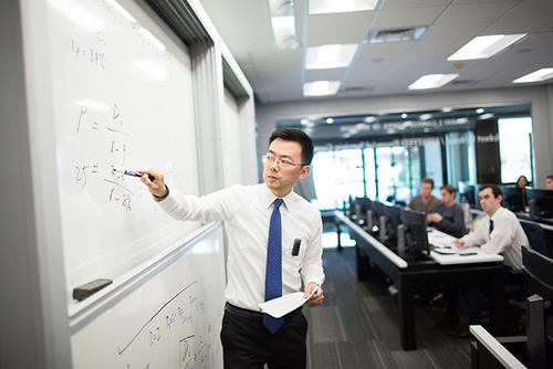 A business professor writing on a whiteboard. 