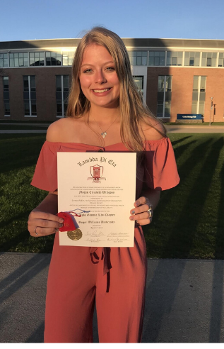 Person standing in front of building holding diploma. 