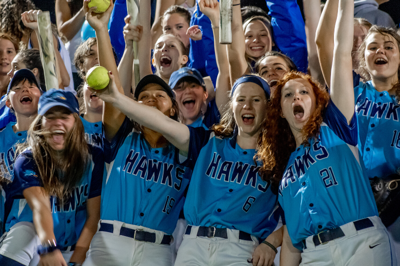 Softball players in Hawks uniforms, cheering. 