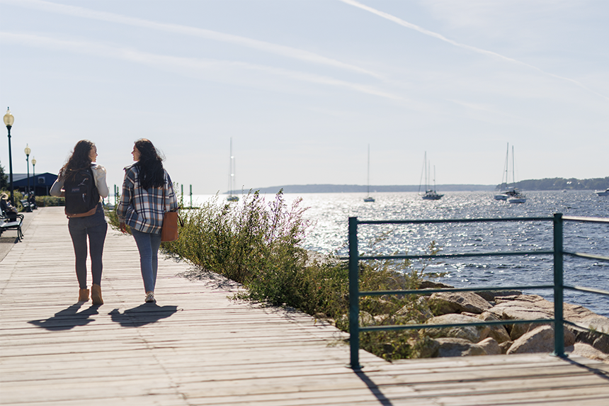 Two people walk along the Bristol harbor