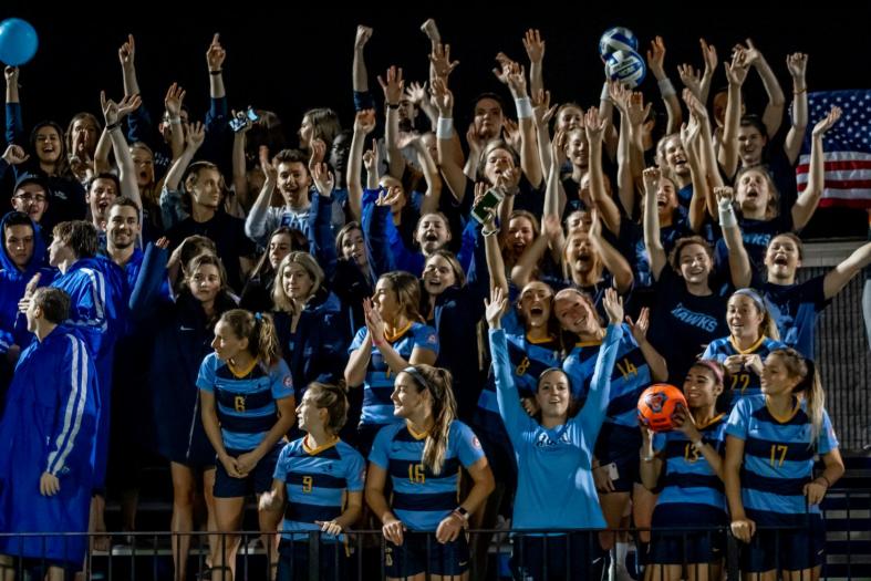 Students from a range of athletic teams, student organizations and clubs fill the turf field bleachers