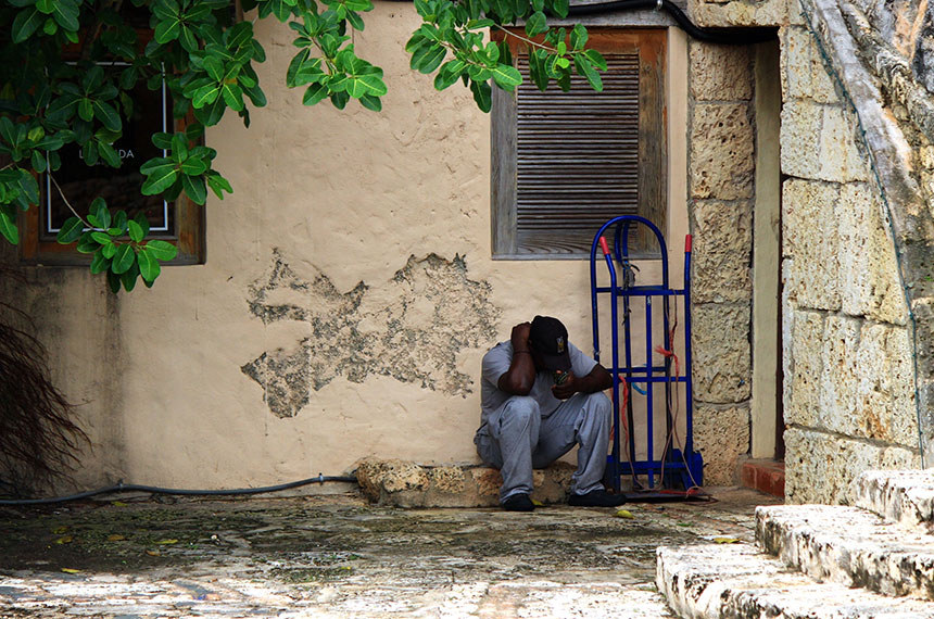 A man is sitting in front of a building looking down with his head in his hands.