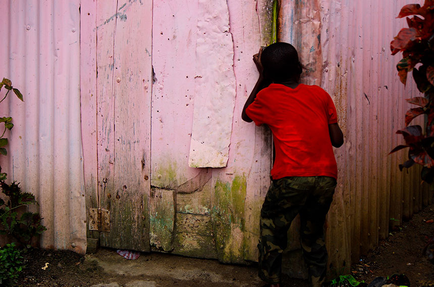 A boy is peaking through a gap in a fence.