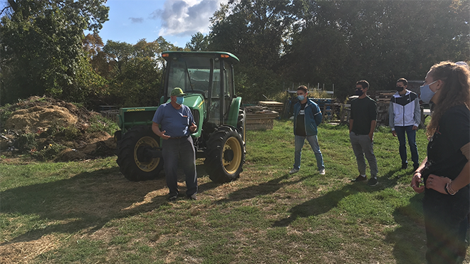 Students stand and listen to a man talking next to a tractor