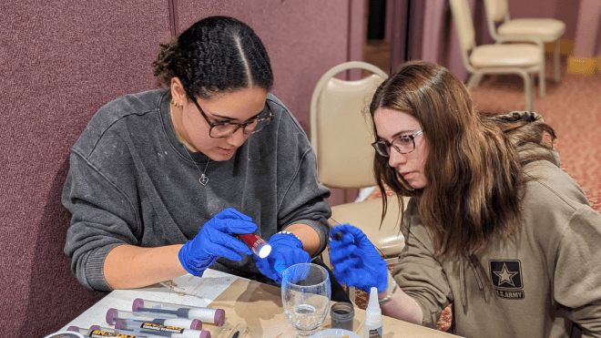 Two RWU students using a blacklight to find fingerprints on a glass cup. 