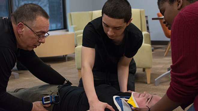 Students at practice placing someone on a stretcher.