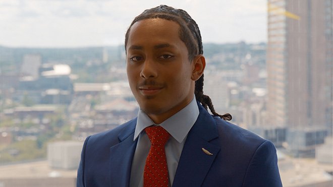 A headshot of Christain Barbosa, who is wearing a blue suit and red tie 