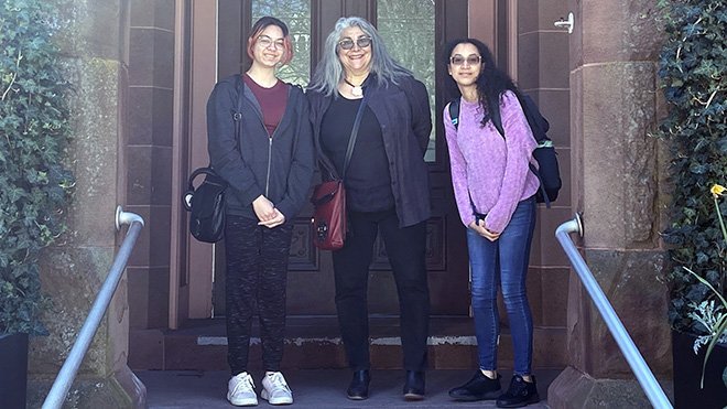 Professor Renee Soto stands on the steps in front of the Rogers Free Library with a Creative Writing student on each side of her