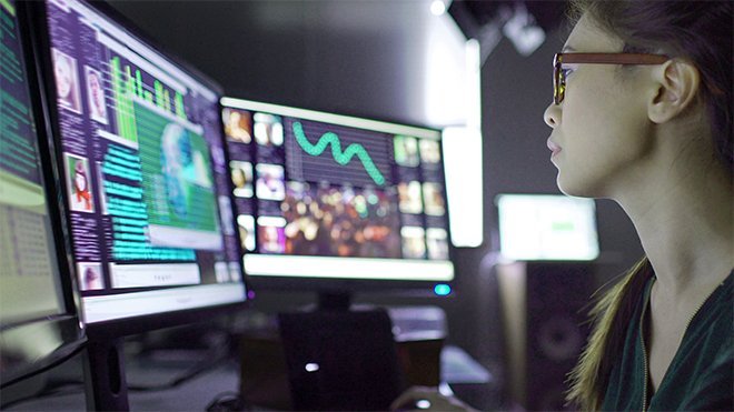 Woman studies data on multiple computer screens.