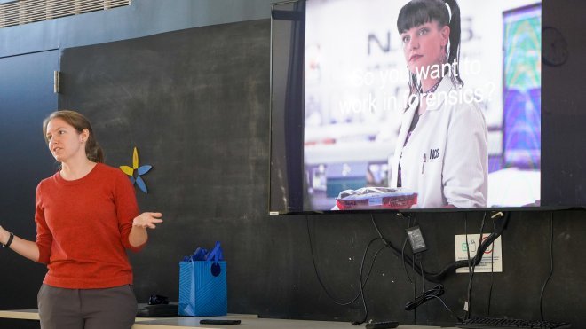 Sarah Lewis, senior forensic scientist at the RIDOH is standing and presenting to the forensic science club about the career track options of forensic scientists. The slide behind her reads "So you want to work in forensics?" and features a photo of Abby from the TV show NCIS.