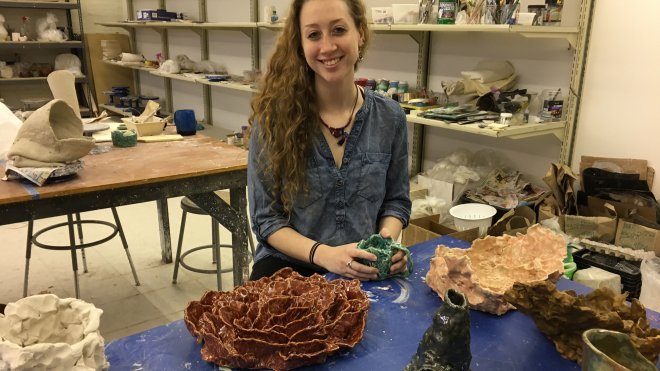 Student seated in the ceramics studio, surrounded by her art.