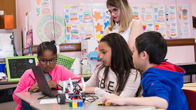 RWU student teacher watches as four students work on a laptop