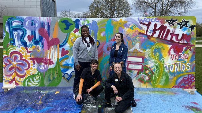 Four people pose in front of the Unity Mural 