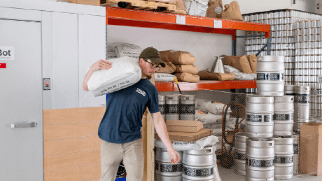 MacConnell carrying bag of malt across brewery. 