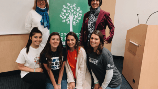 Students posing with guest speakers in front of Sandy Hook Promise sign. 