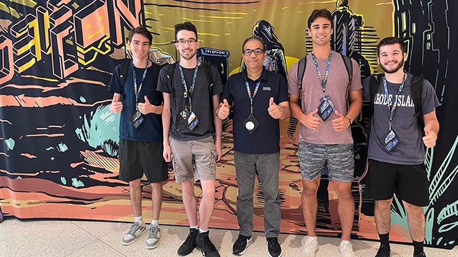 Shakour Abuzneid with four RWU students posing for a photo in front of a wall that says "Def Con"