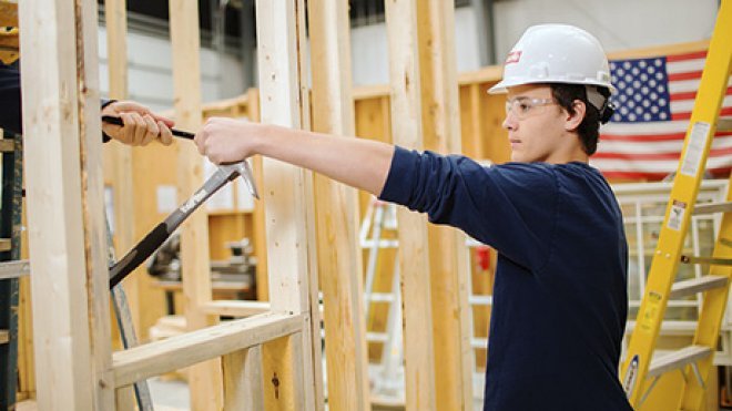 Construction management student at a construction site handing off a tool.