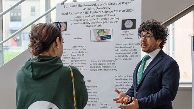 A student stands in front of a poster and talks with another student at SASH