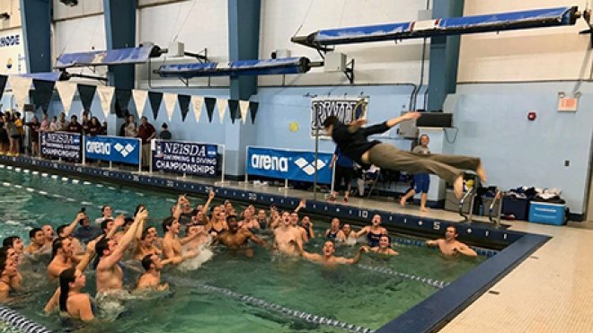 A student dives into a pool while his teammates celebrate their victory.