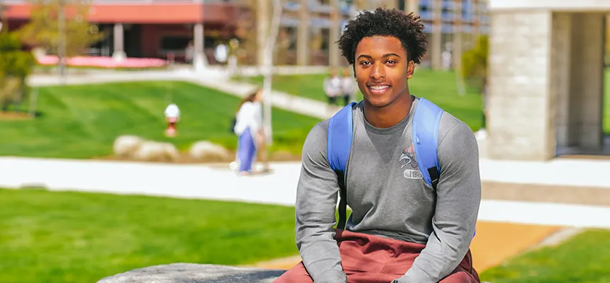Students sits on a bench on the Bristol campus and smiles at the camera
