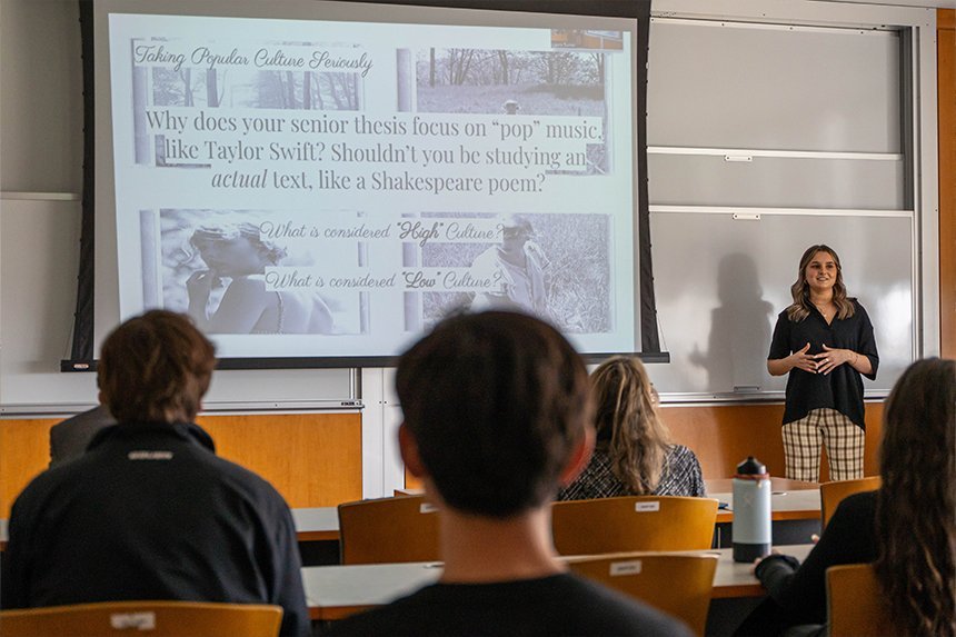 A student standing next to a big screen with her project slides 