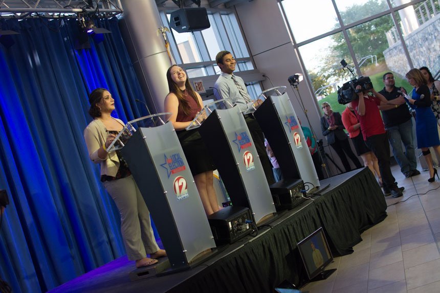 Students stand on stage at podiums. 