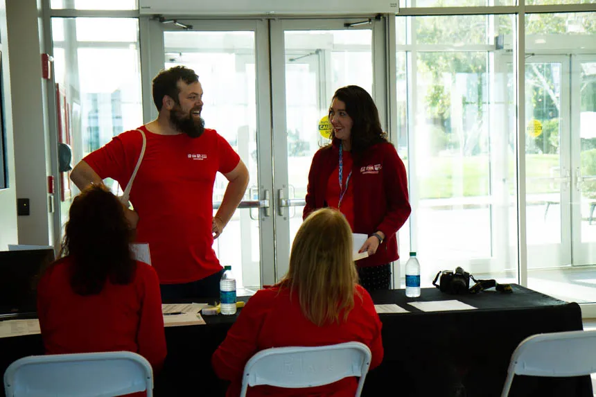 Four news crew members in red shirts gather around a table. 