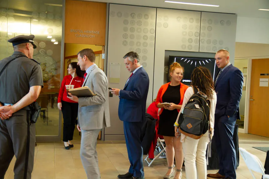 A group of people stand, smiling and talking to one another. 