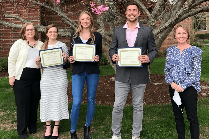 Five people stand outdoors, three of them holding certificates