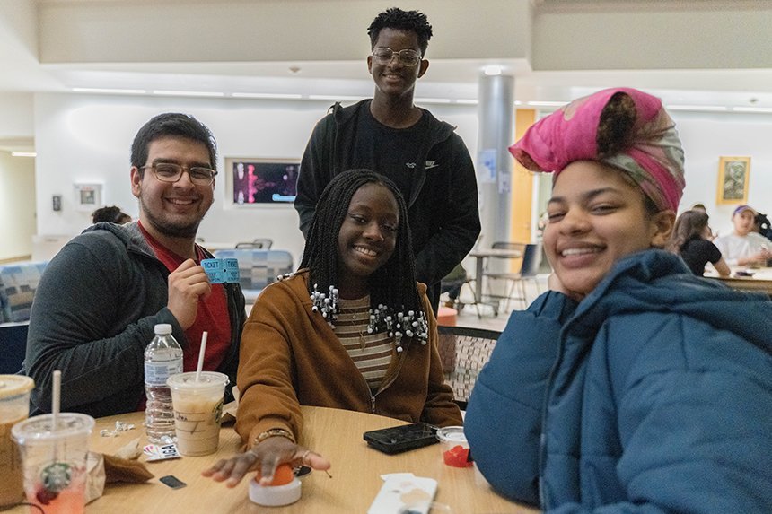 Four students, three sitting and one standing, around a table at the Jeopardy event.