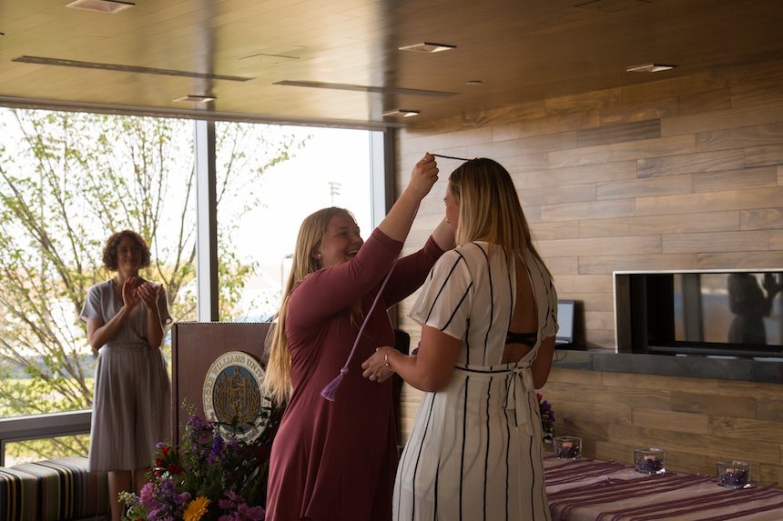 student placing graduation cord around another student