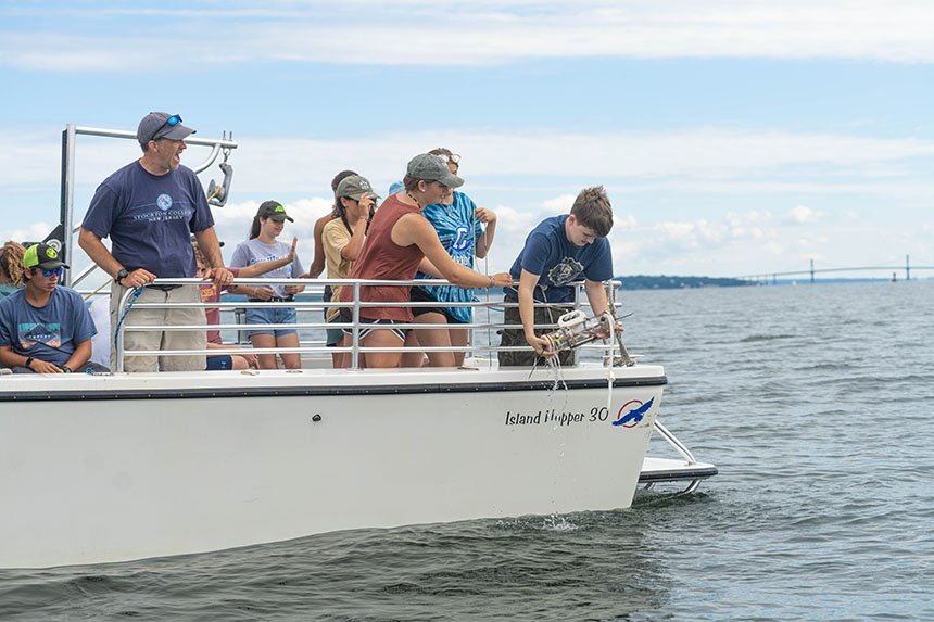 A student lowering a water collection device into Mount Hope Bay.