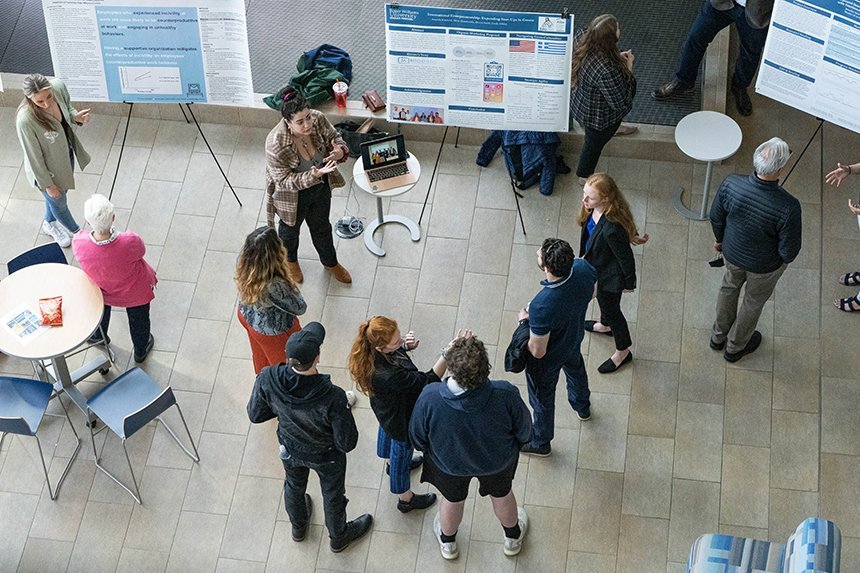 A group of people listen to a student presenting at SASH 