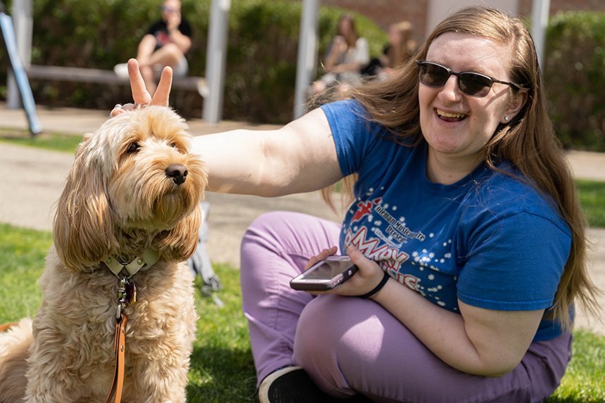 A student sitting on Commons Quad with a dog. 