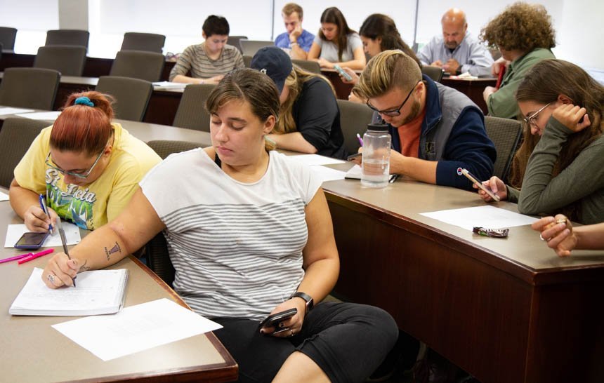 Students research on cell phones and take notes. 