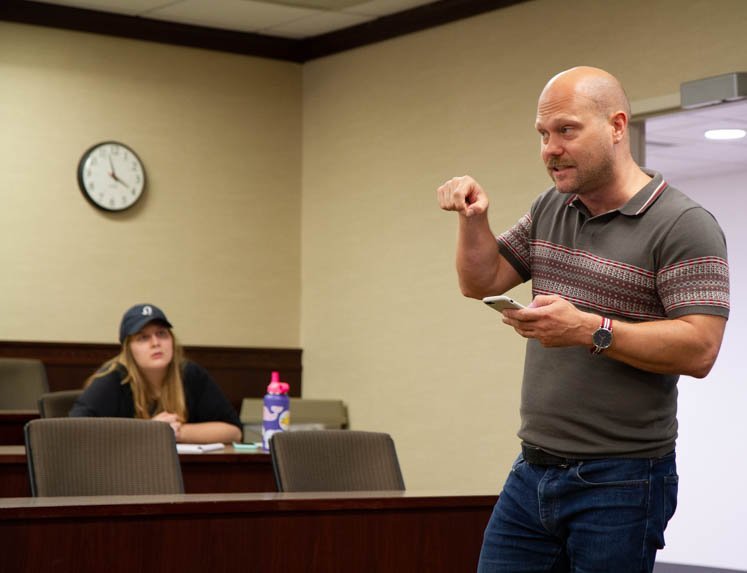 A presenter performs a poem while a student looks on. 