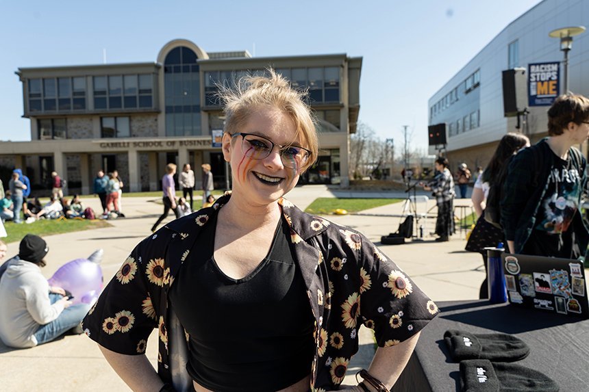 A student standing outside with rainbow face paint on their cheeks. 